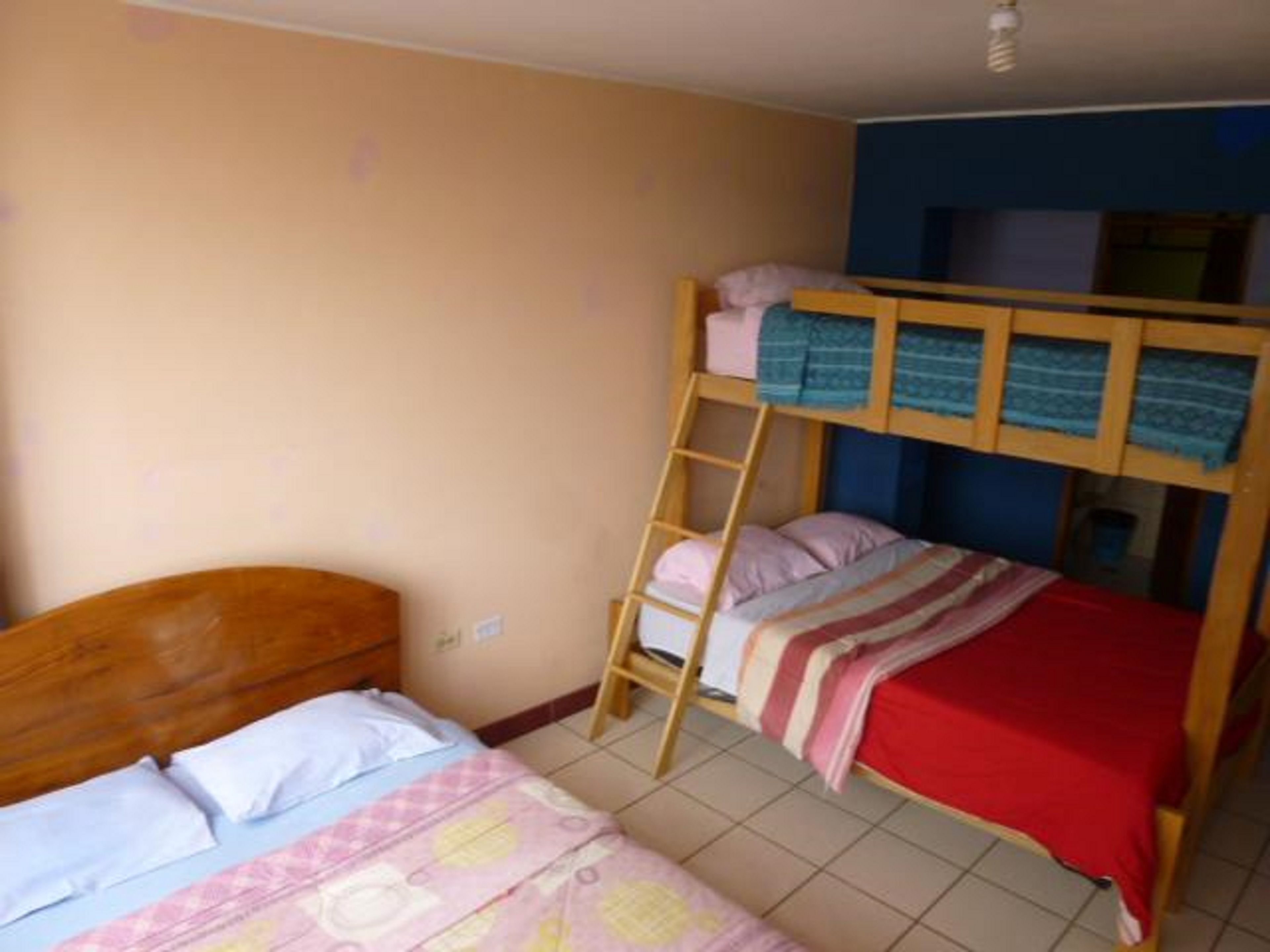 A dormitory room with bunk beds, a wooden ladder, and a tiled floor.