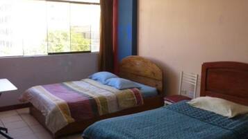 Un dormitorio con dos camas, una ventana con cortinas, una silla y un escritorio.