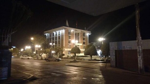 Un edificio de varios pisos con una torre central, iluminado por farolas.
