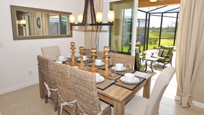 Un coin repas avec une table en bois dressée pour six personnes, entourée de chaises en osier. Un grand miroir est accroché au mur, au-dessus de la table.