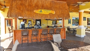 A bar area with a thatched roof, bar stools, and a sign for 'Land Shark Lager'.