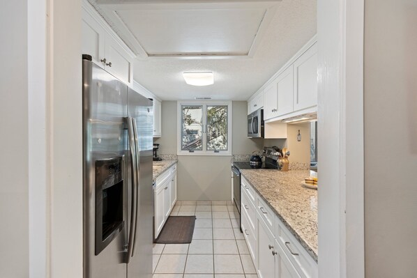A compact kitchen with white cabinets, stainless steel appliances, and a granite countertop.