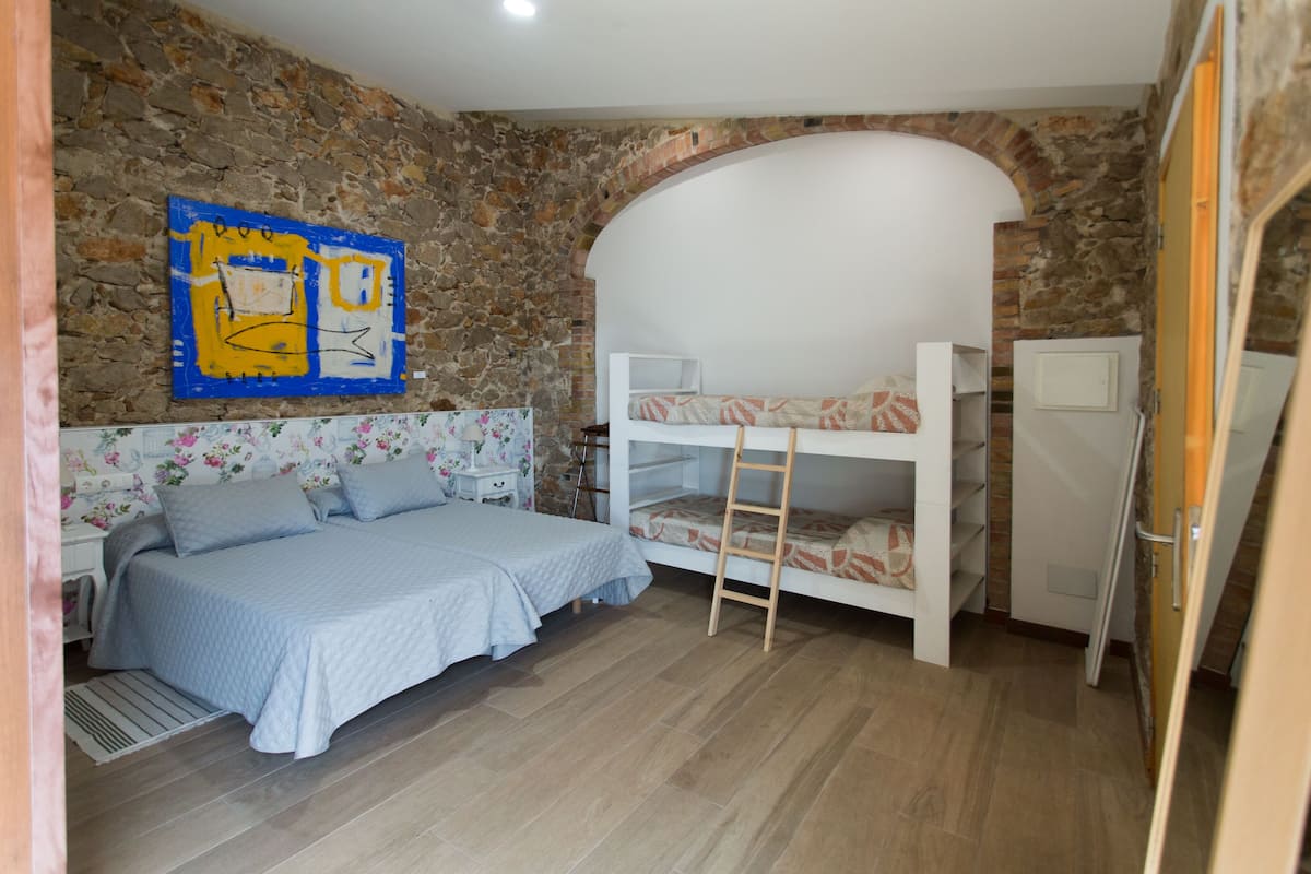 A bedroom with a bunk bed, a single bed, a stone wall, and a painting.