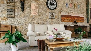A cozy living room with a stone wall, a clock, a couch, and various decorative items. - Cortijo Cal Rajoler (Cabanes)