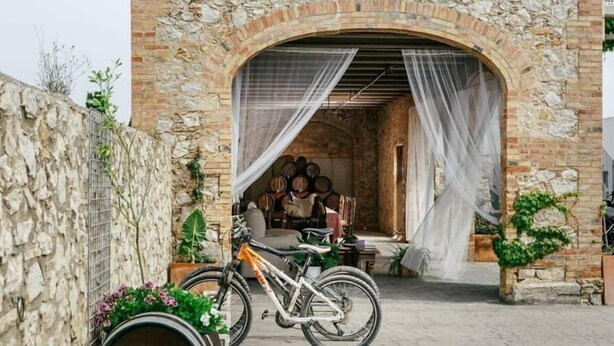 A stone building with a rustic archway, a bicycle, and barrels. - Cortijo Cal Rajoler (Cabanes)