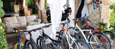 Un espacio exterior cubierto con zona de estar, una mesa blanca, un sofá y varias bicicletas aparcadas.