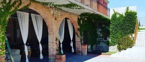 A building with a stone facade, arched windows, and a covered outdoor area with white curtains.