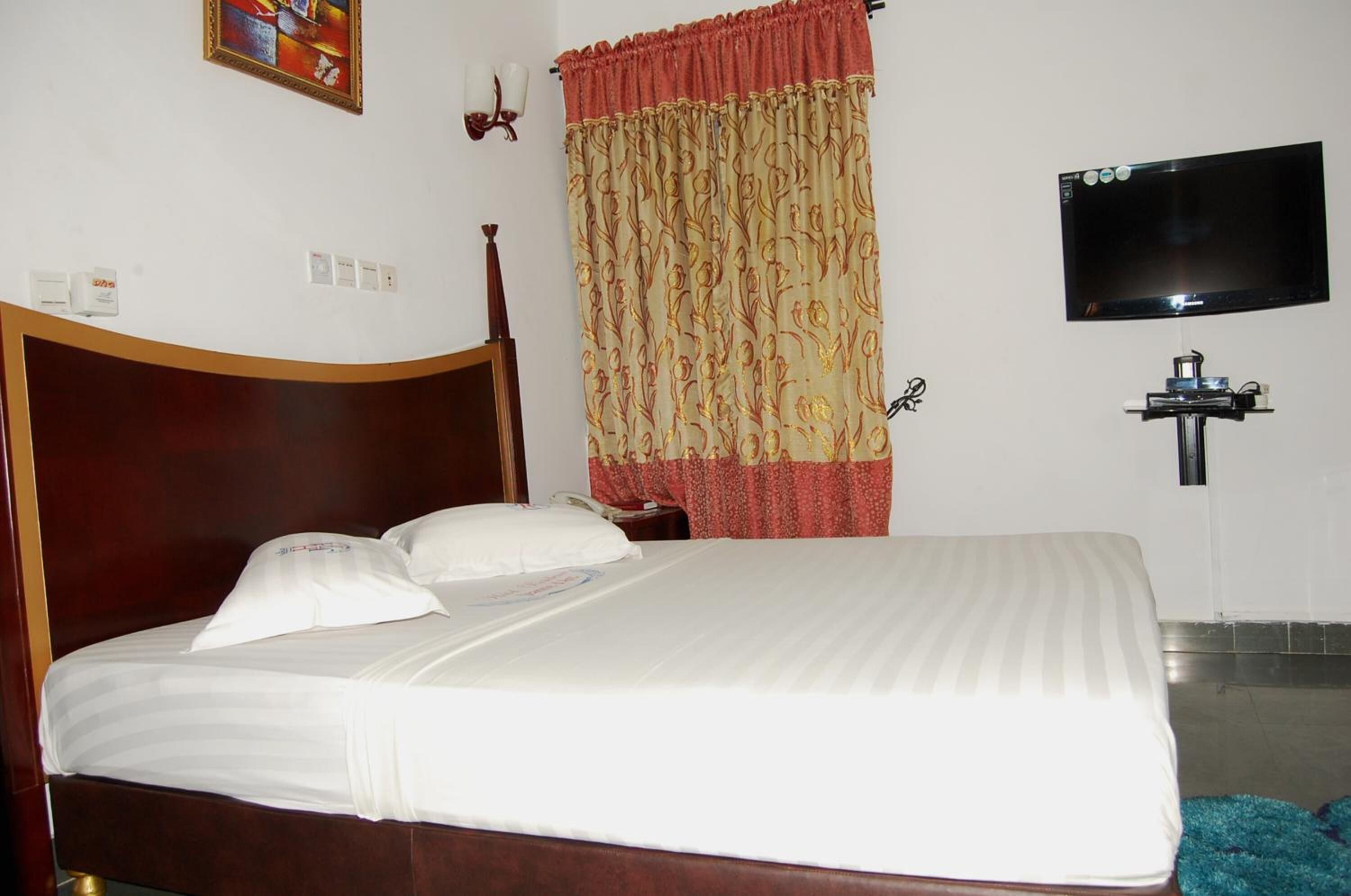 A hotel room with a wooden bed, a television mounted on the wall, and a curtain with a floral pattern.