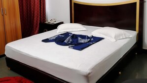 A neatly made bed with white linens and a blue garment on it. There is a painting on the wall above the bed. - Hotel Paramondo (Abomey-Calavi)