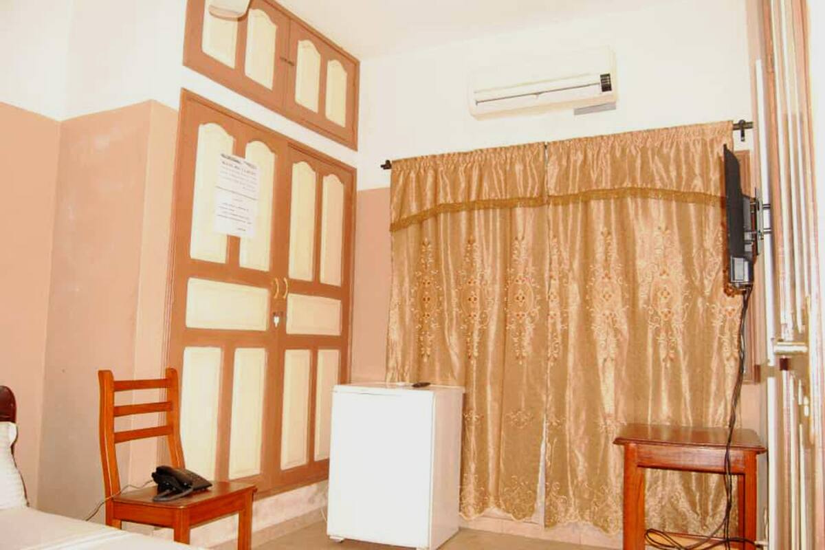 A room with a wooden door, a white refrigerator, a desk with a chair, and a curtain.