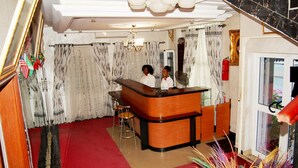 A reception area with a wooden counter, two bar stools, and a red carpet. - Hotel Paramondo (Abomey-Calavi)