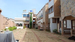 A courtyard with a paved walkway, buildings with balconies, and a table with a tablecloth. - Hotel Paramondo (Abomey-Calavi)