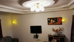 A living room with a flat-screen TV, two sofas, a coffee table, a cabinet, and a ceiling light fixture. - Hotel Paramondo (Abomey-Calavi)