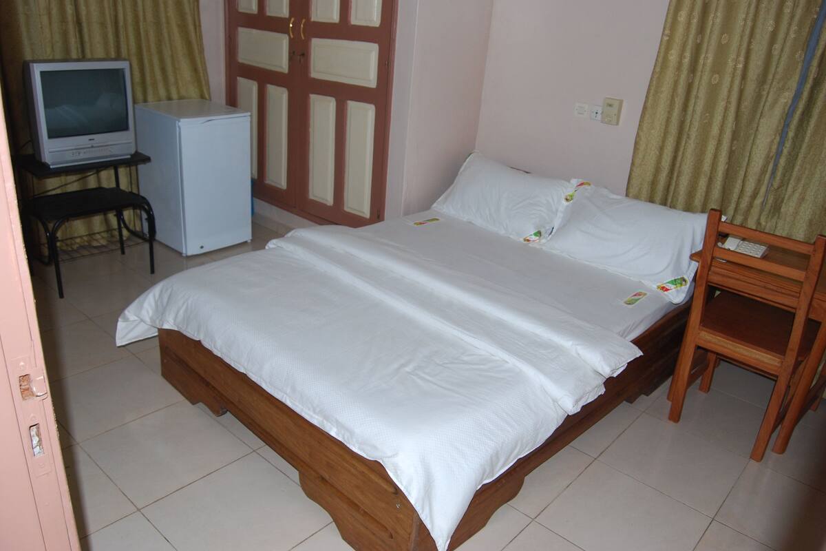 A bedroom with a single bed, a small desk with a television, and a wardrobe.