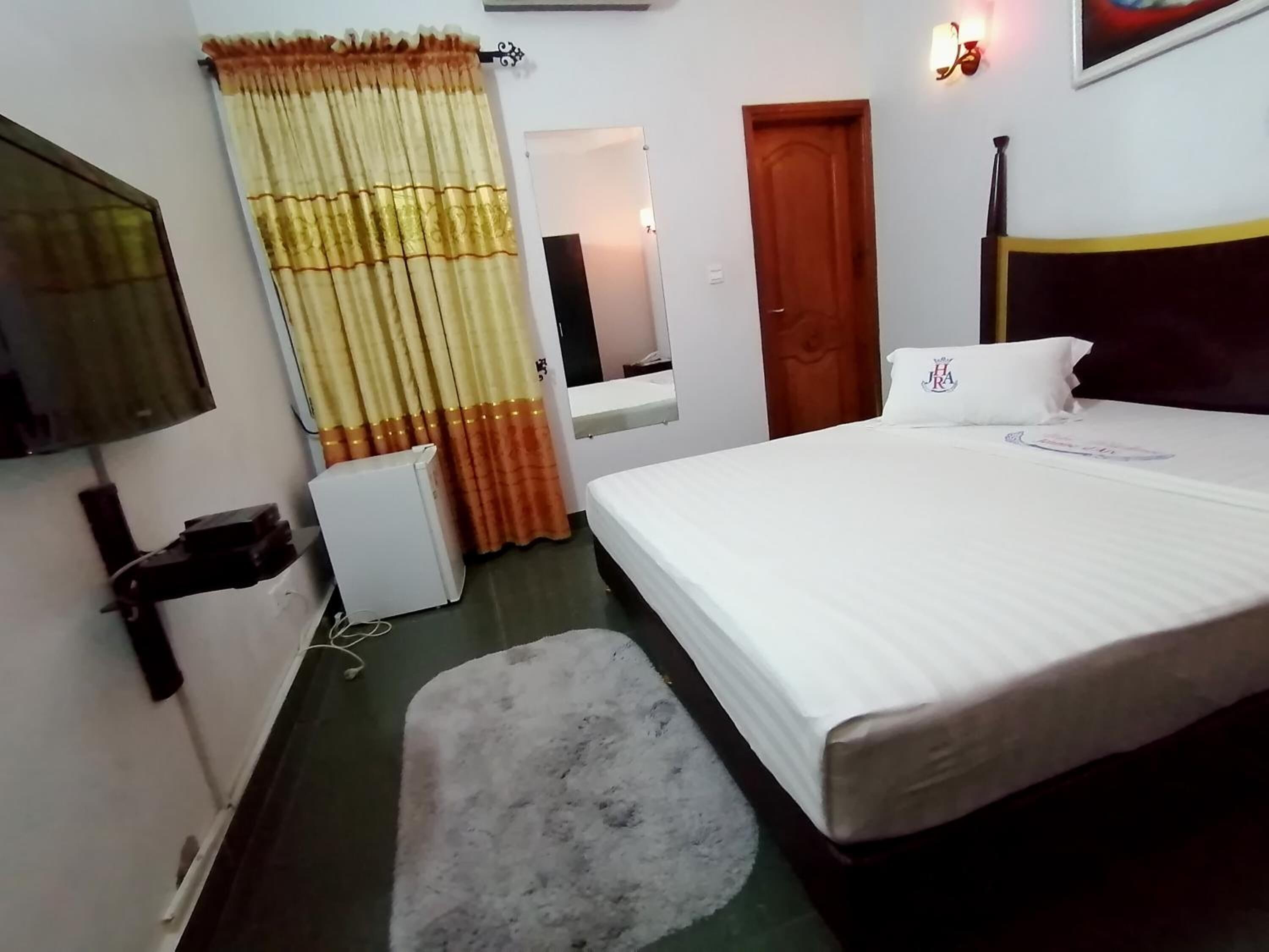 Una habitación de hotel con cama, escritorio pequeño, espejo, puerta y cortina.