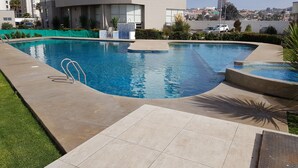 A swimming pool with a tiled deck, surrounded by a landscaped area with grass and plants. - Lunoma Departamento (Coquimbo)
