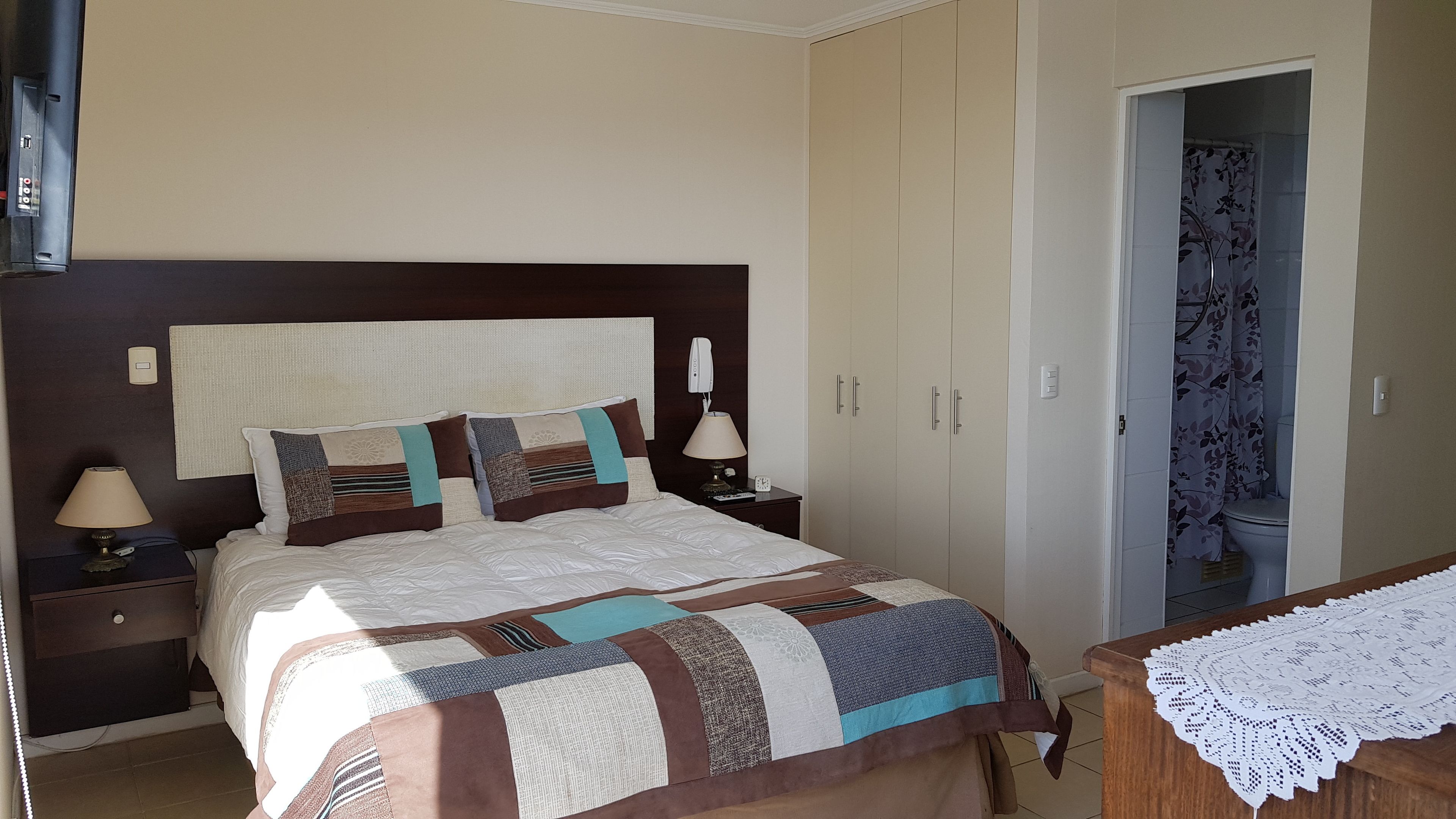 A neatly made bed with a patterned bedspread and pillows, a bedside table with a lamp, and a wardrobe with a mirror.