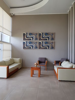 A modern living room with a beige sofa, two armchairs, a small wooden table with a vase, and abstract wall art.