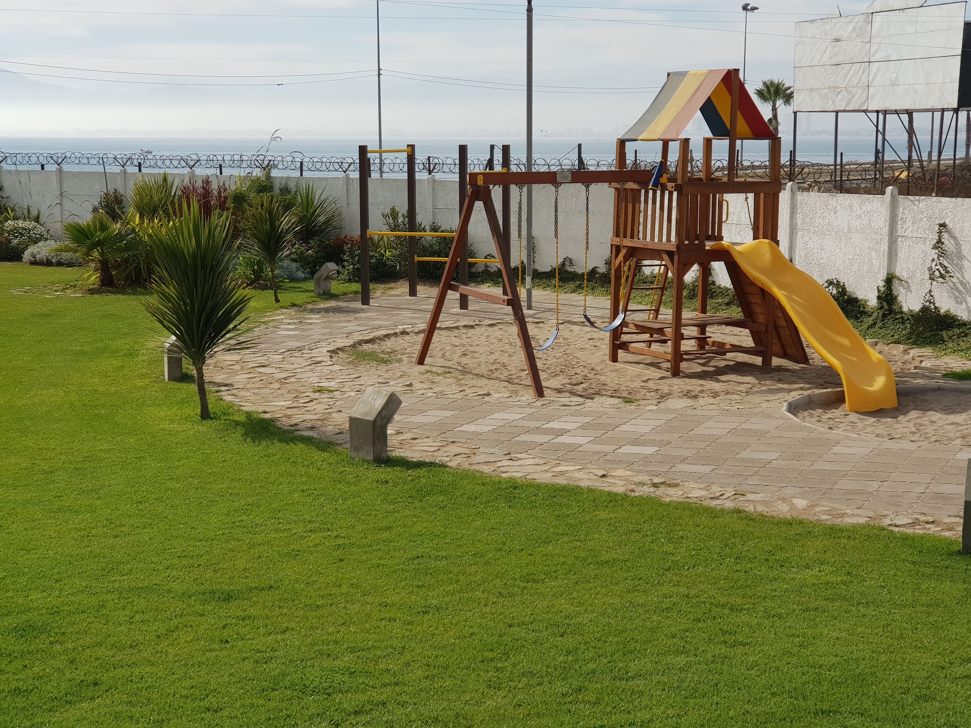 Une aire de jeux avec un toboggan, des balançoires et une structure d’escalade, située près d’une plage.