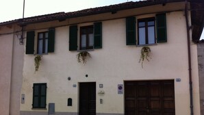 A building with a beige facade, green shutters, and a large wooden door. - Ai Cappuccini (Racconigi)
