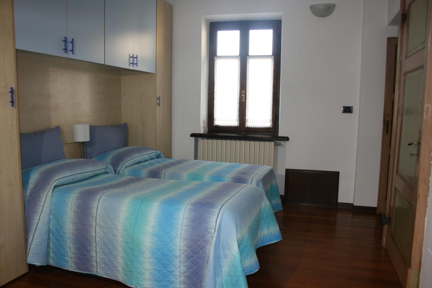 A room with two beds, a window, and a radiator.