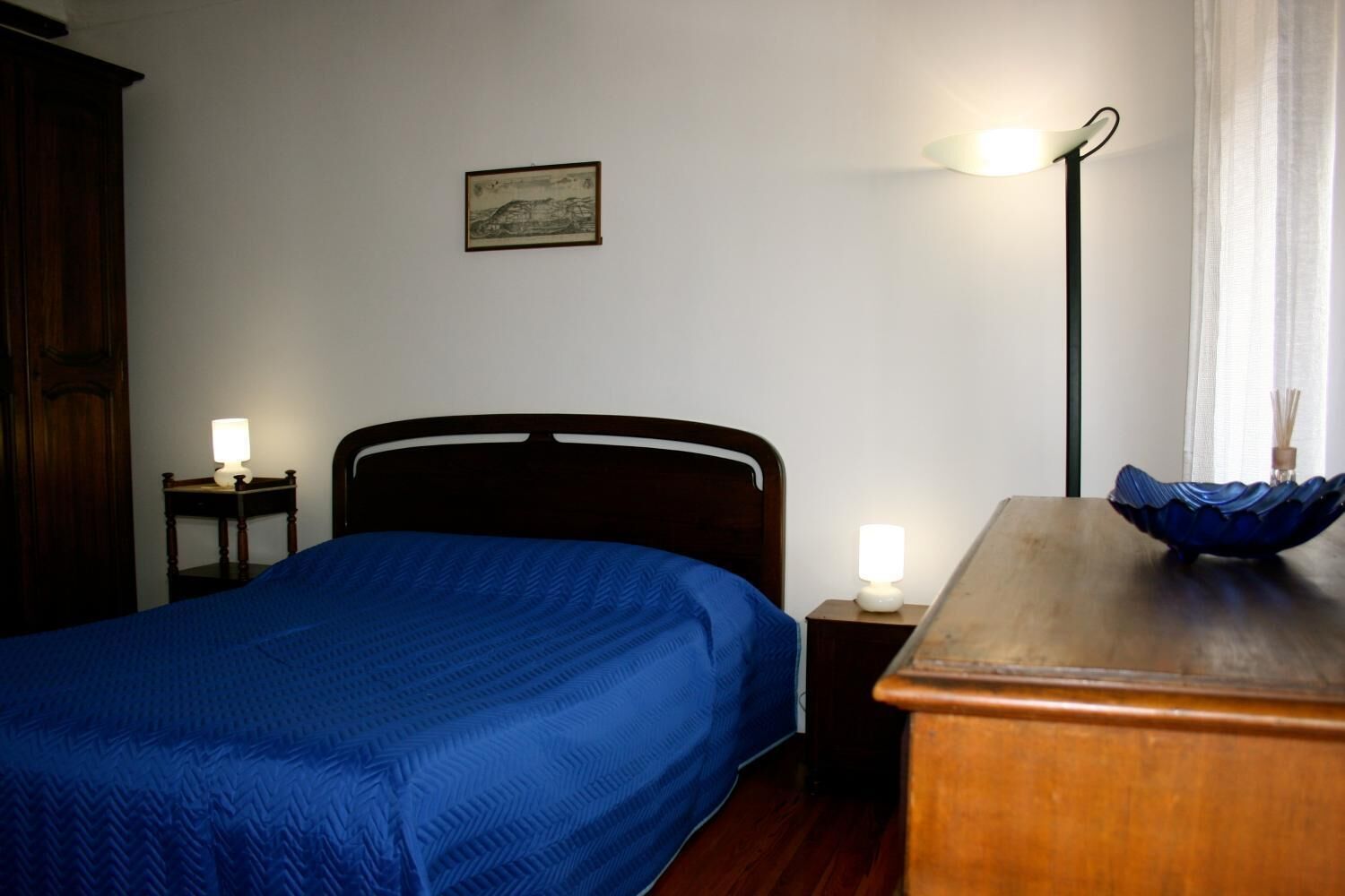 A bedroom with a bed, bedside tables, a lamp, a picture on the wall, and a window with curtains.