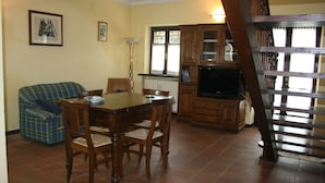 A dining area with a wooden table and chairs, a sofa, and a staircase. - Ai Cappuccini (Racconigi)