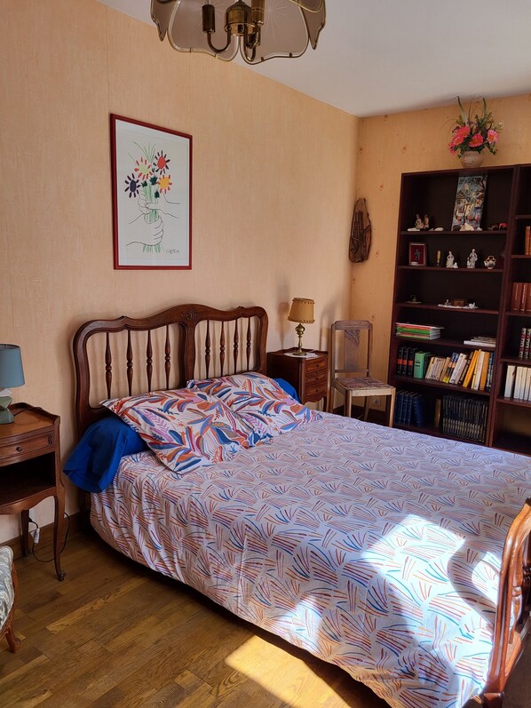 A bedroom with a wooden bed, a bookshelf, a desk, and a wall-mounted lamp. - House in Royan From The Park, 5 Minutes From The Beach (Royan)