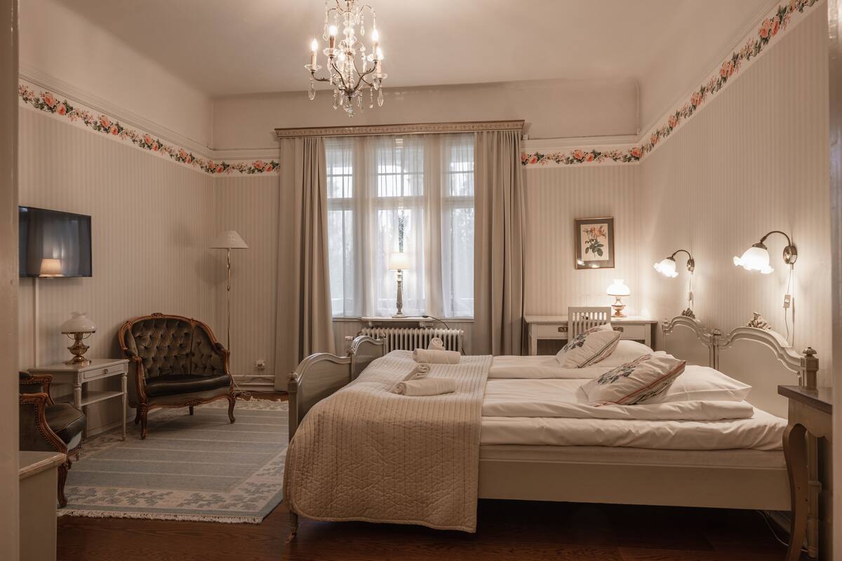 A classic bedroom with a large bed, a chair, a desk, and a chandelier.