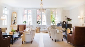 A spacious living room with a grand chandelier, comfortable seating, and large windows with floral views. - Korstäppans Herrgård (Leksand)