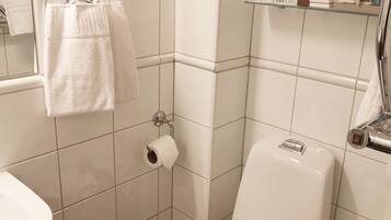 A small bathroom with white tiles, a toilet, a sink, and a towel rack.