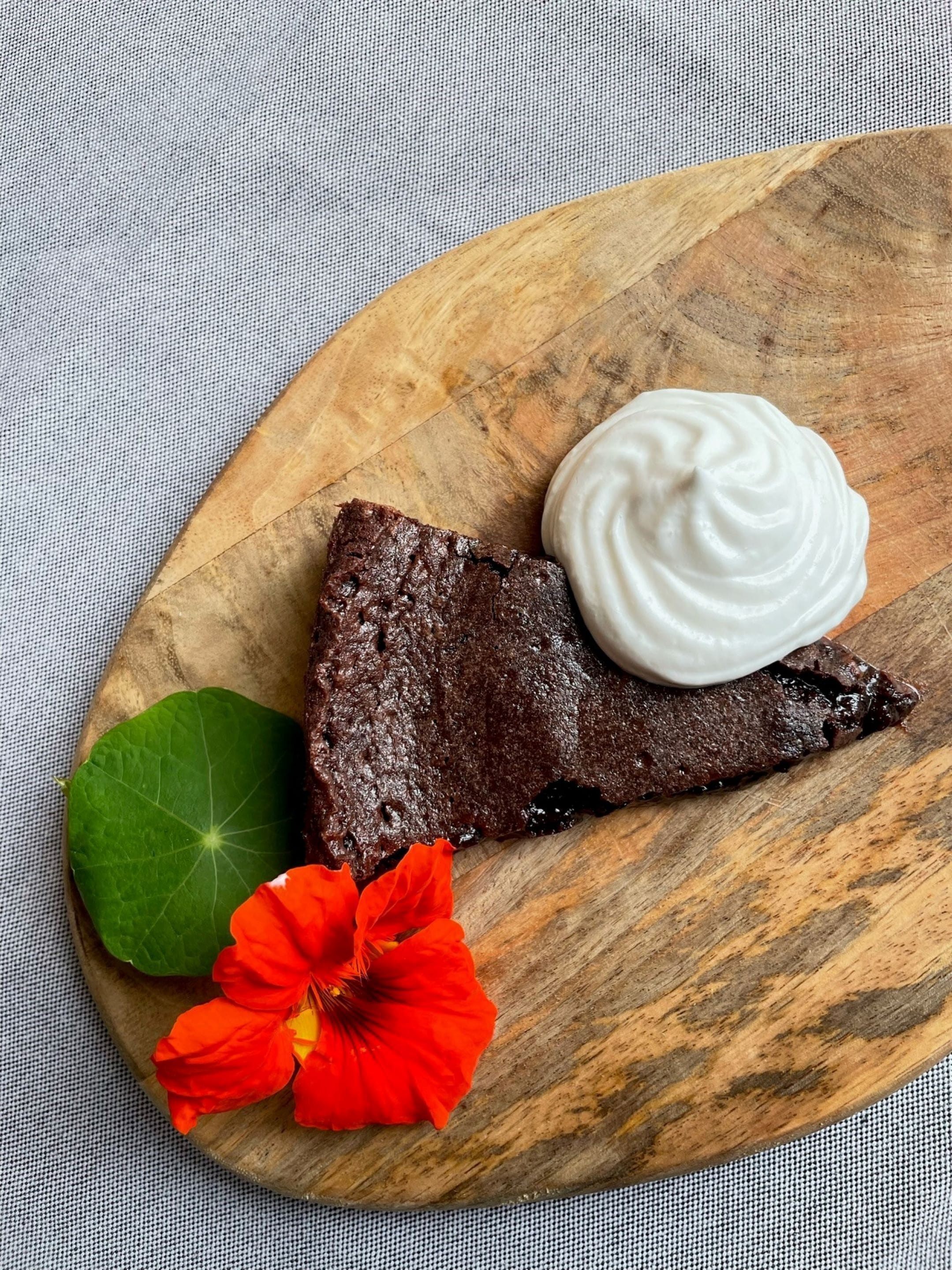 A slice of chocolate cake with whipped cream on a wooden board.