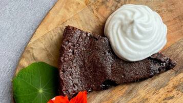 A slice of chocolate cake with whipped cream on a wooden board.