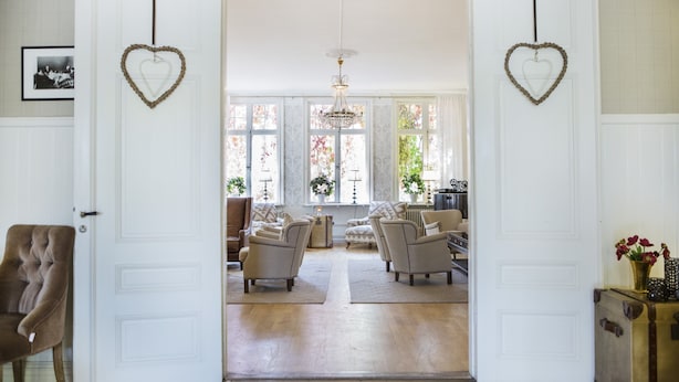 An open doorway leading to a living room with two armchairs, a chandelier, and a view of a garden through large windows. - Korstäppans Herrgård (Leksand)