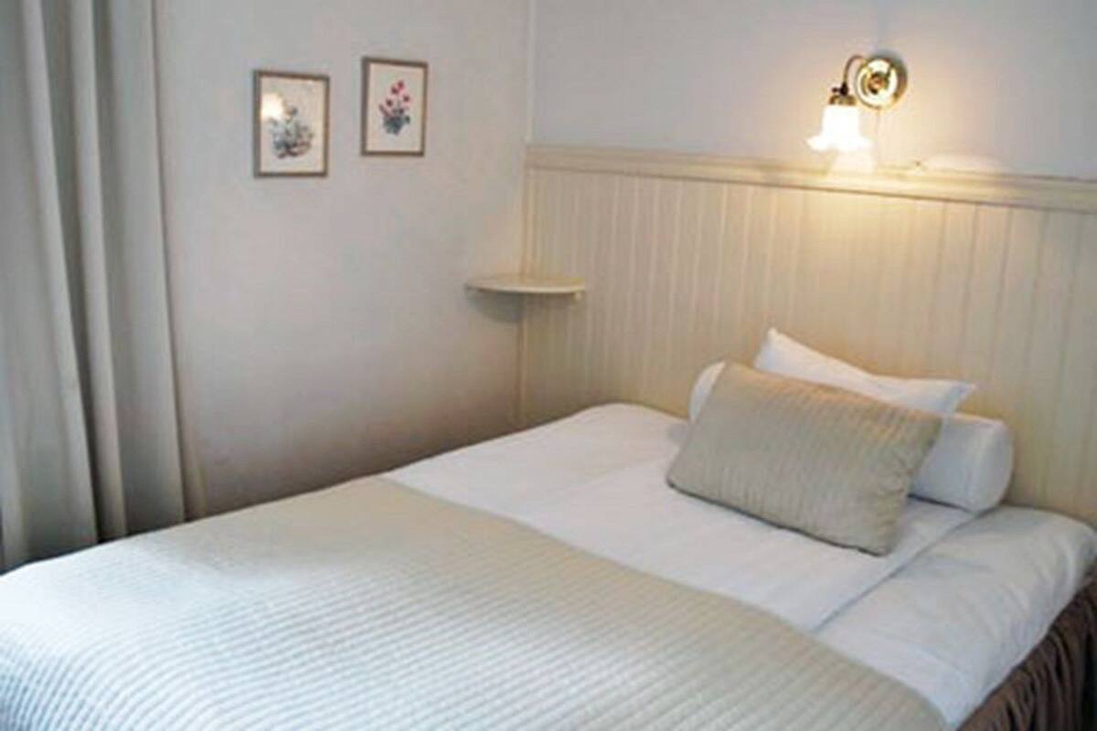 A hotel room with a bed, a nightstand, a wall-mounted light, and two framed pictures.