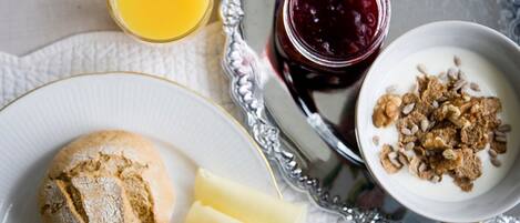 A breakfast tray with a croissant, cheese, a bowl of cereal with nuts, a glass of orange juice, and a jar of jam.