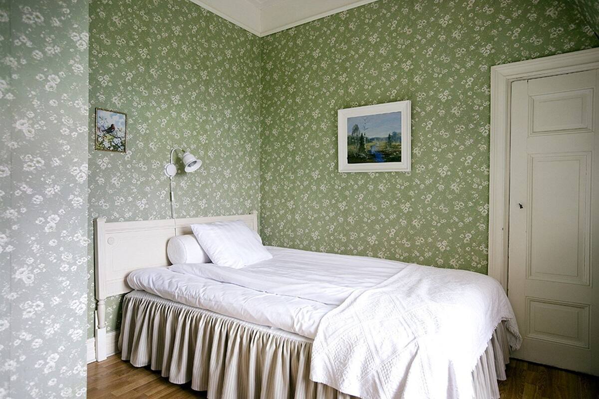 A bedroom with a bed, a nightstand, a wall-mounted lamp, and two framed pictures.