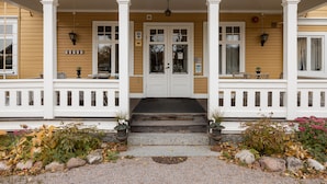 A two-story house with a porch, a front door, and a small garden area with rocks and plants. - Korstäppans Herrgård (Leksand)