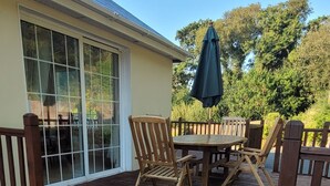Un patio con terraza de madera, una mesa y sillas, y un ventanal grande.