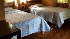 A room with two wooden beds, a wooden table, and a window with curtains. - Finca el Refugio de Papito (El Molino)