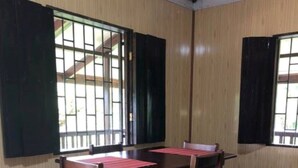 A room with a wooden floor, a table with chairs, and windows with black shutters. - Finca el Refugio de Papito (El Molino)