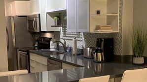 A modern kitchen with stainless steel appliances, a central island with bar stools, and a tiled backsplash. - Beautiful Studio on the Beach at The Decoplage (Miami Beach)