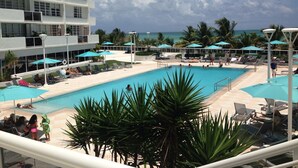 A pool area with lounge chairs and umbrellas, overlooking a body of water. - Beautiful Studio on the Beach at The Decoplage (Miami Beach)