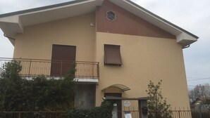 A two-story building with a beige facade, a small balcony with a metal railing, and a gated entrance. - Casa Salice (Racconigi)