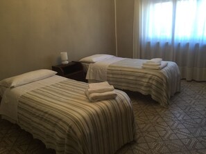 Two single beds with striped bedding, a bedside table with a lamp, and a patterned floor. - Casa Salice (Racconigi)