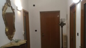 A hallway with a patterned floor, a wooden door at the end, a mirror on the left, and a candelabra on the right. - Casa Salice (Racconigi)