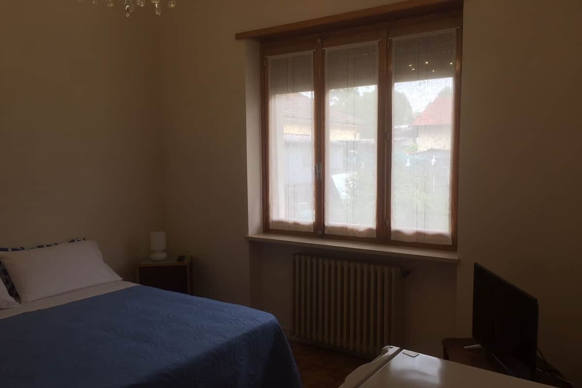 A bedroom with a bed, a desk, a radiator, and a window with blinds.