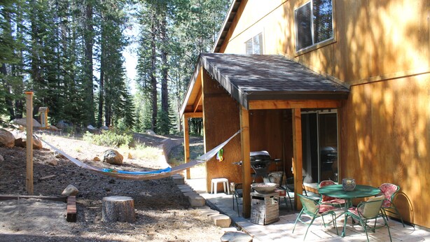 Una baita in legno con un'area patio che include un tavolo, sedie, un'amaca e un barbecue.