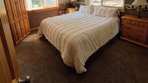 Camera da letto con un letto grande, due comodini, una cassettiera e un armadio. Due finestre offrono luce naturale e vista sugli alberi.