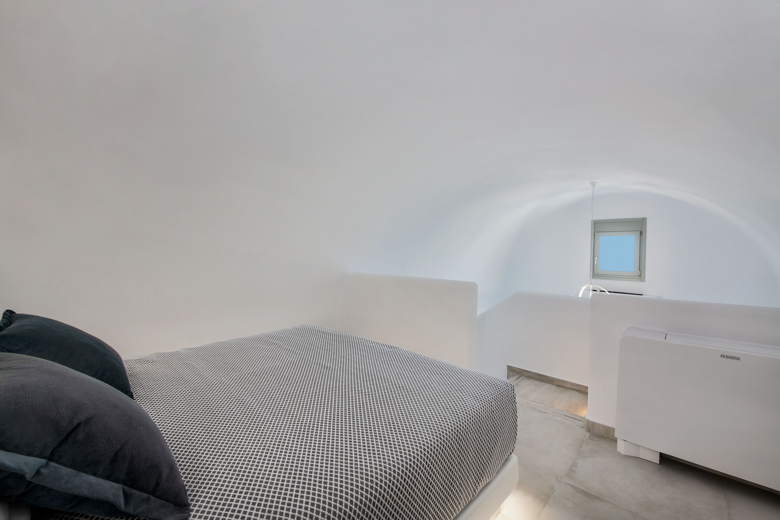 A minimalist room with a bed, a small window, and a white radiator.